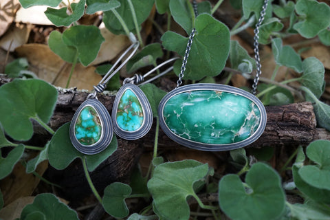 a picture of a pair of turquoise earrings and necklace resting in greenery