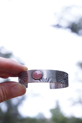 image of a silver wrist cuff with stamped flower patterns and a pink faceted stone.