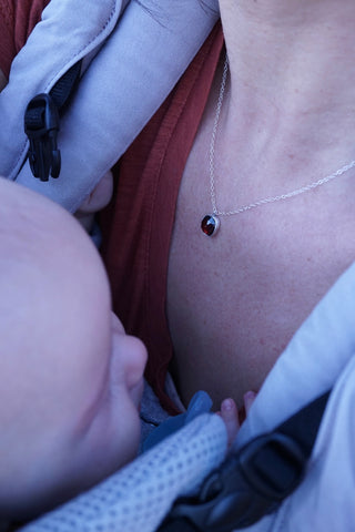 A small child in a front carrier with a visible garnet necklace on the mother
