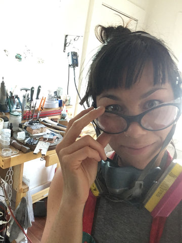 erika wearing protective glasses and respirator looking at camera at her workbench