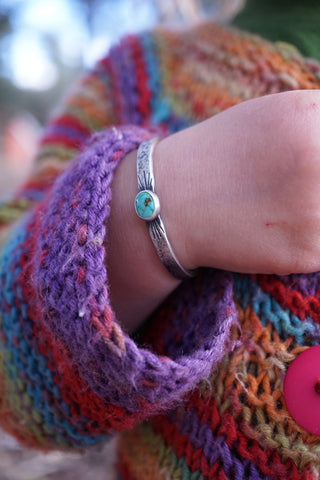 a picture of a toddler's wrist with a silver and turquoise baby cuff