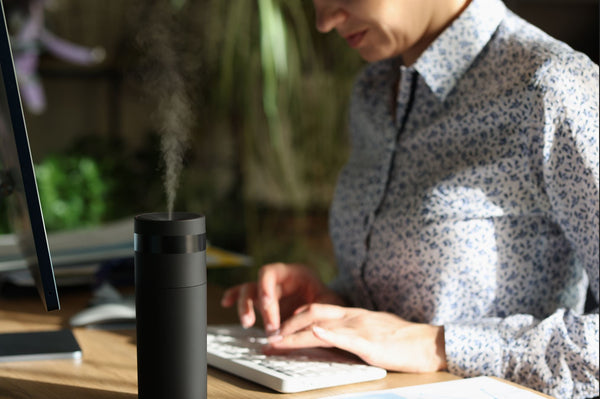 Woman at a computer researching and a diffuser operating in the foreground