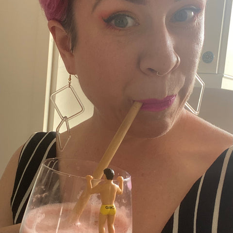 Alison from WildBird Studio drinking out of a straw. There is a little man holding onto the edge of her glass with pants that say Chad