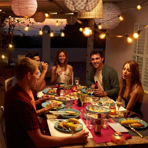 Personas cenando en una terraza. Una guirnalda de luz ilumina ell espacio.