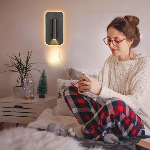 Lámpara encendida pegada a la pared. Al lado derecho hay una mujer en pijama cargando su celular a la entrada USB de la lámpara.