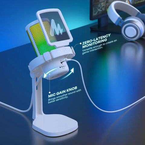 Micrófono blanco con luz LED de color verde y amarillo, sobre escritorio. A la derecha superior de la imagen hay unos audífonos blancos recargados sobre una pantalla.