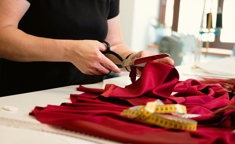 A person using a pair of scissors to manually cut a piece of red fabric