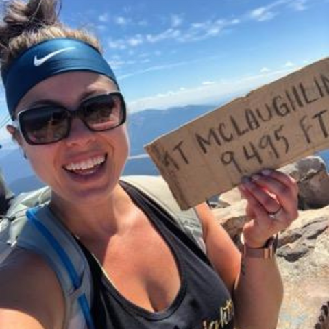 woman smiling at top of mountain, holding sign with elevation