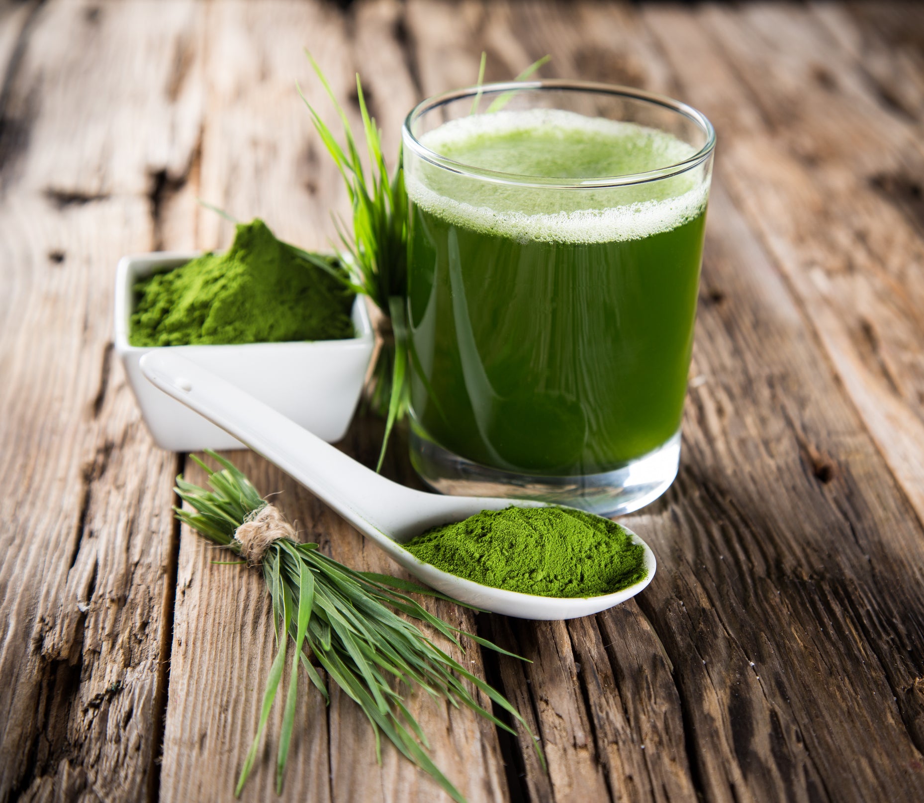A glass of wheatgrass juice with a bunch of wheatgrass