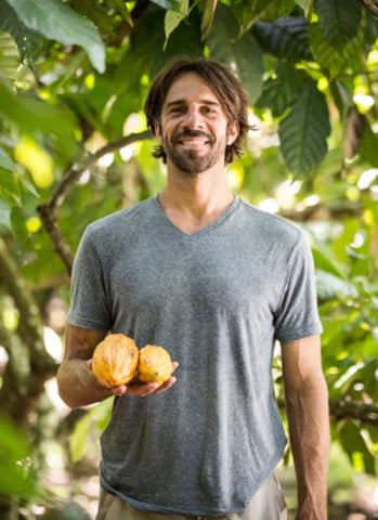 To'ak co-founder Jerry Toth stands holding two yellow cacao pods with a smile on his face