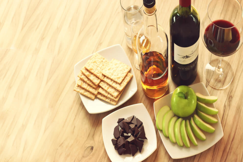 a plate of chocolate pieces sits beside apple slices, crackers, wine, and whiskey