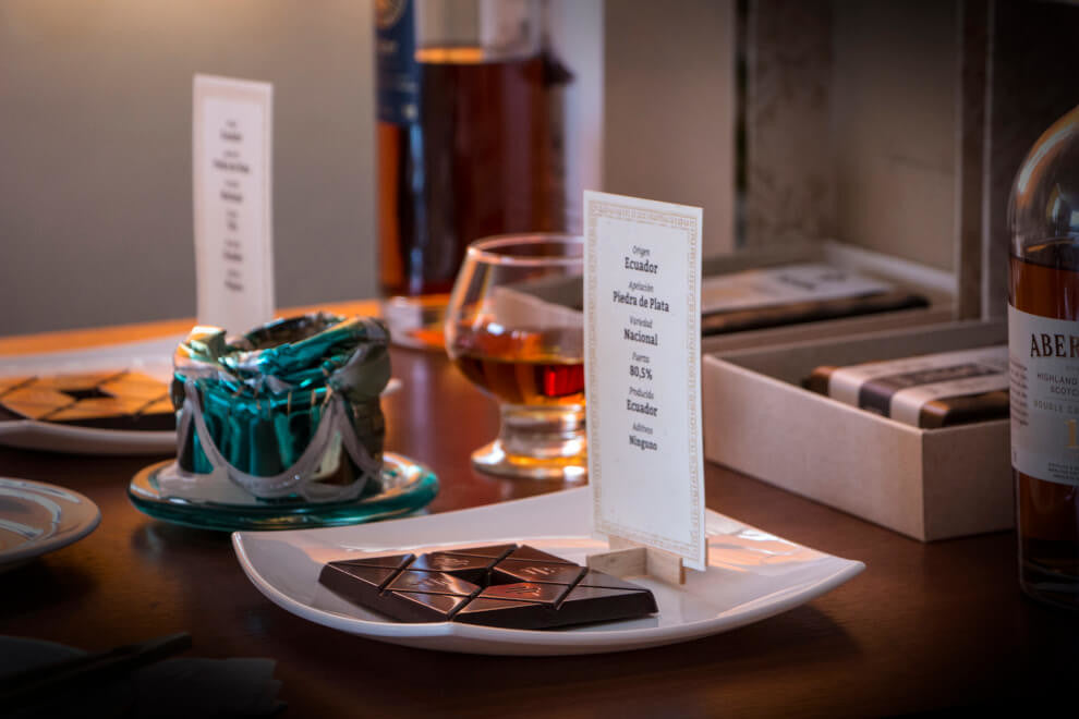 a bar of To'ak Chocolate sits on a plate beside a glass of whiskey 