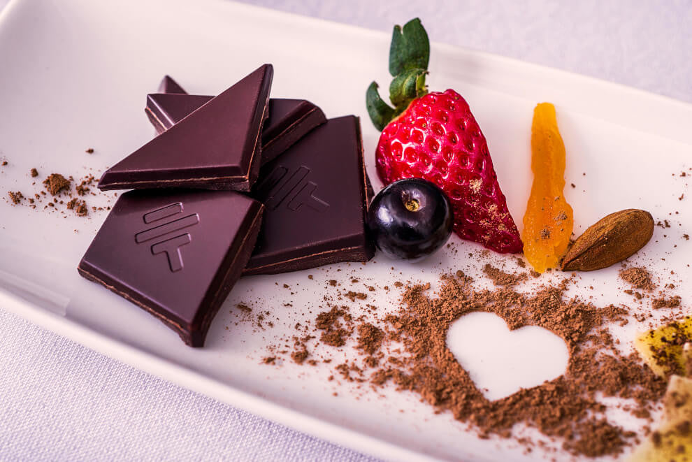 pieces of To'ak Chocolate sit on a white plate beside a sliver of strawberry and a blueberry
