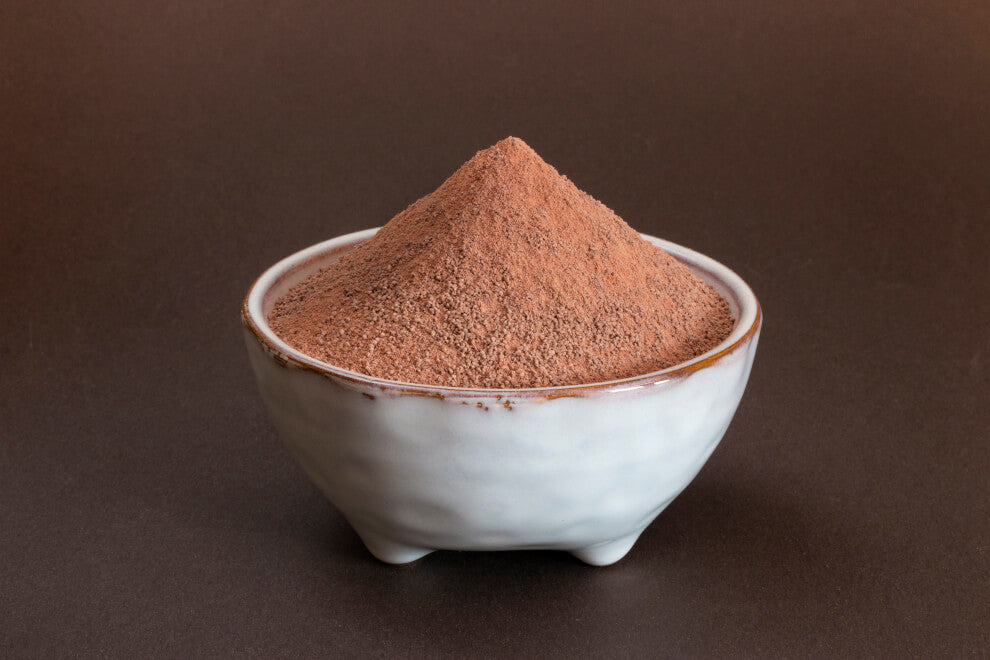 cacao powder sits in a white bowl on a brown background