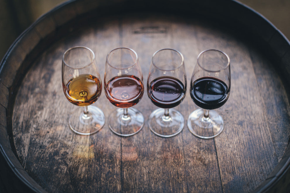 Four glasses containing different wines sit atop a wooden barrel