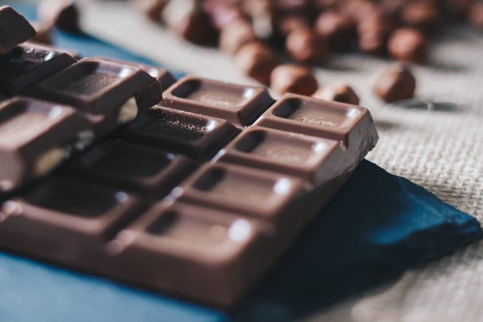 a bar of milk chocolate in the foreground with nuts, blurred, in the background