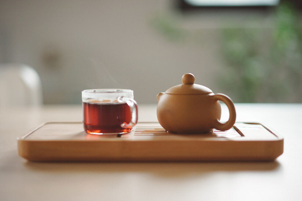 a small brown teapot sits beside a glass cup filled with tea