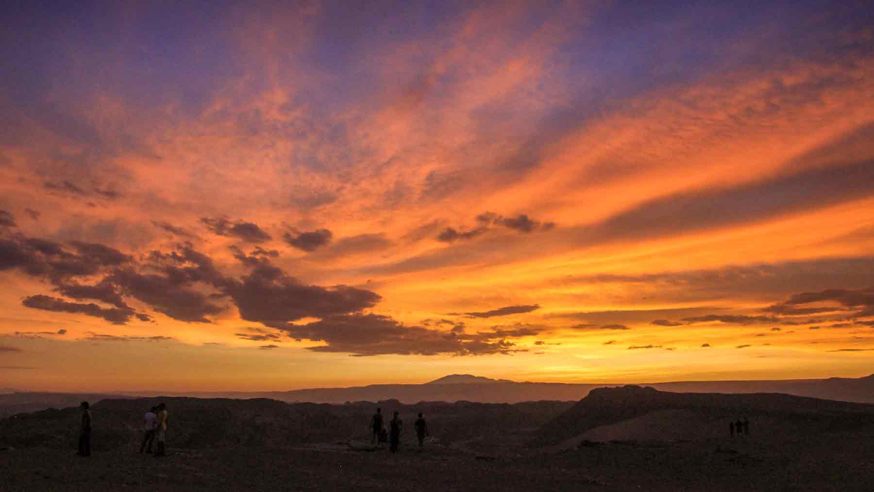 Bright orange sunset over the dark shadows of the Valle De La Luna in Chile, part of the travel that inspired the creation of Asmuss. 