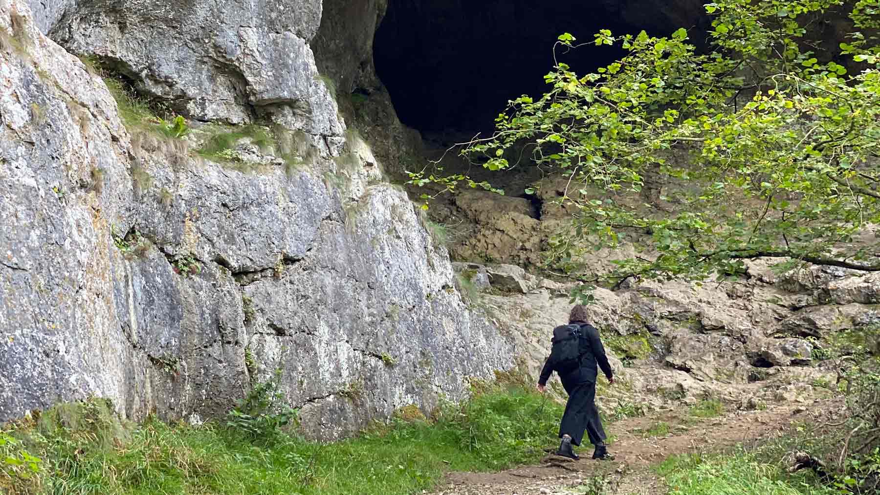 Clare walking near a cave next to the River Dove in the Peak District wearing the Asmuss Wide Leg Trousers and Pleated Zip Through Sweat