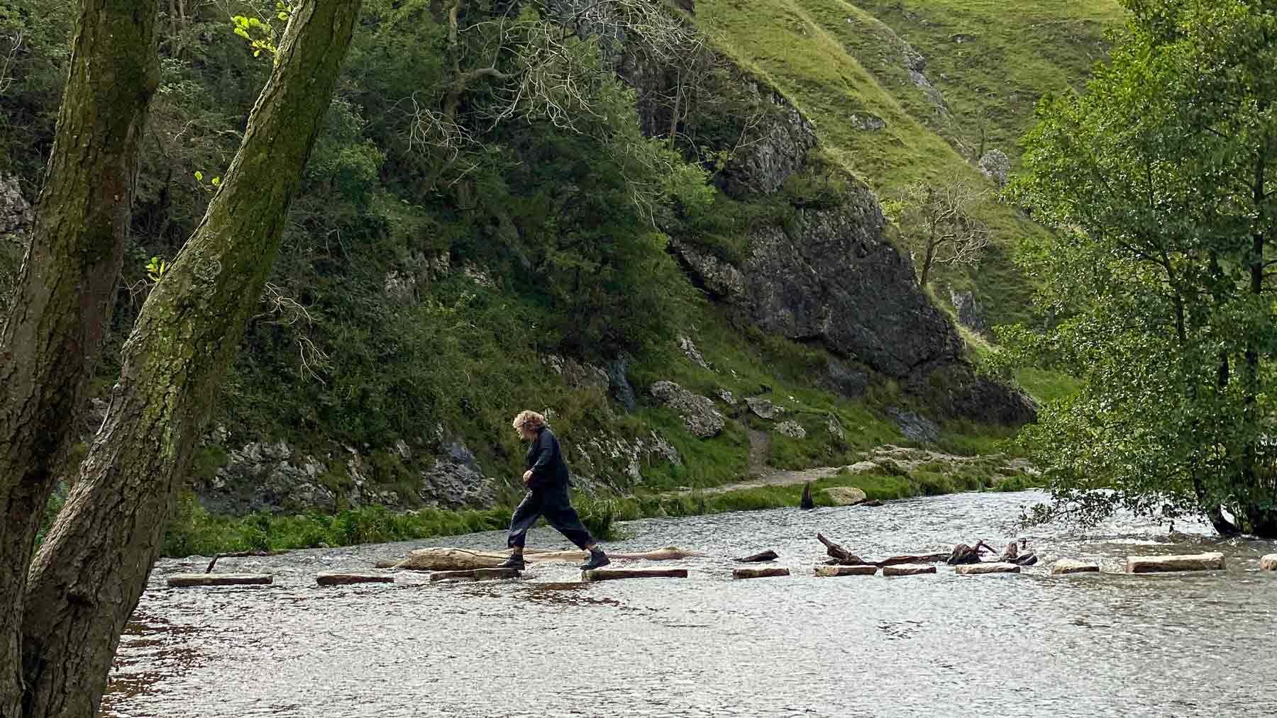 Clare crossing the Dovedale Steeping Stones, wearing Asmuss, in the Peak District