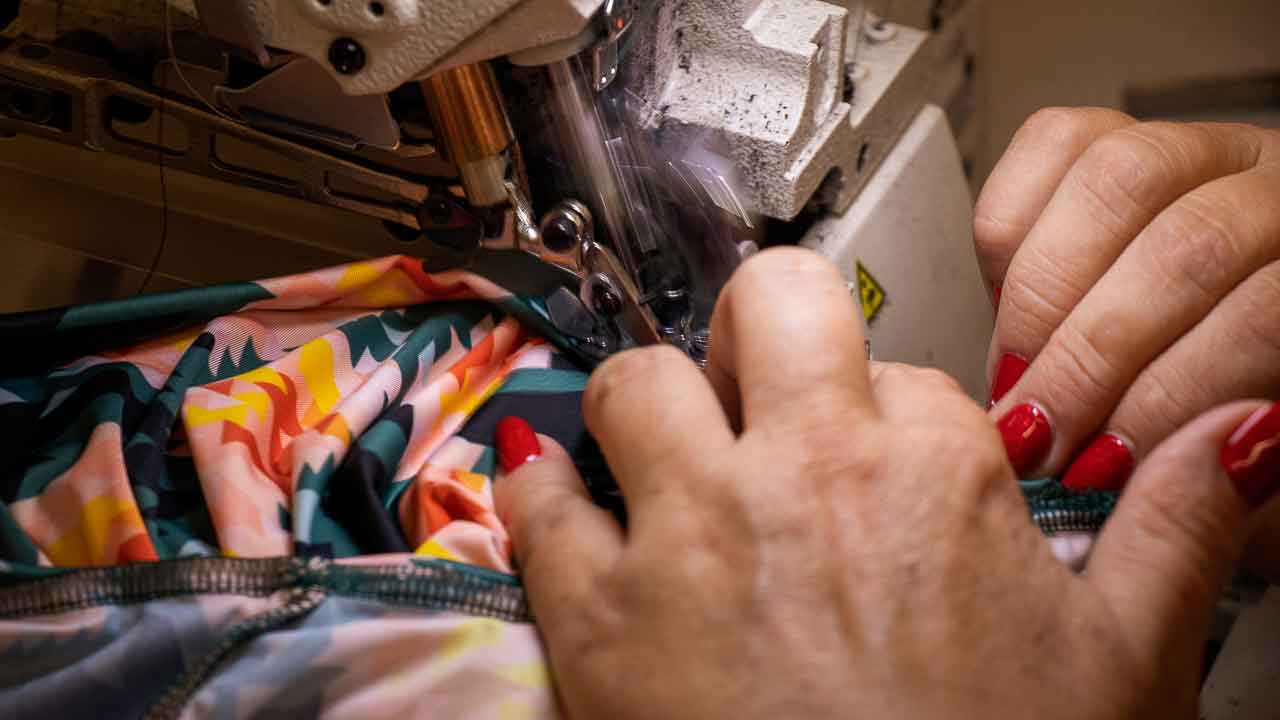 Machinist with bright red finger nails sewing the Asmuss Geo. Rose T-shirt