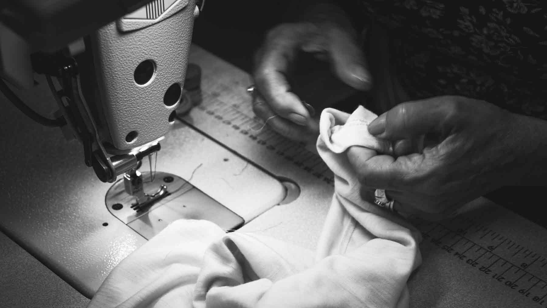 Black and white photo of a sewing machine and the hands of one of the people making one of the Asmuss designs in London