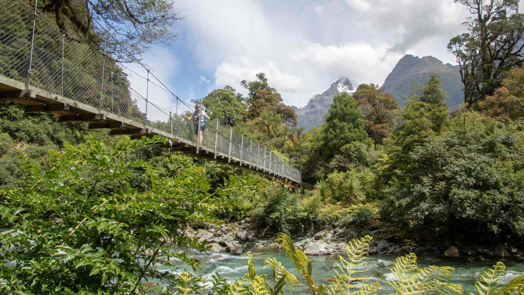 One of many swing bridges on the Hollyford Track.  The Asmuss founders sister is crossing the swing bridge wearing Asmuss luxury travel clothing designs, Hollyford Track, Fiordland, New Zealand