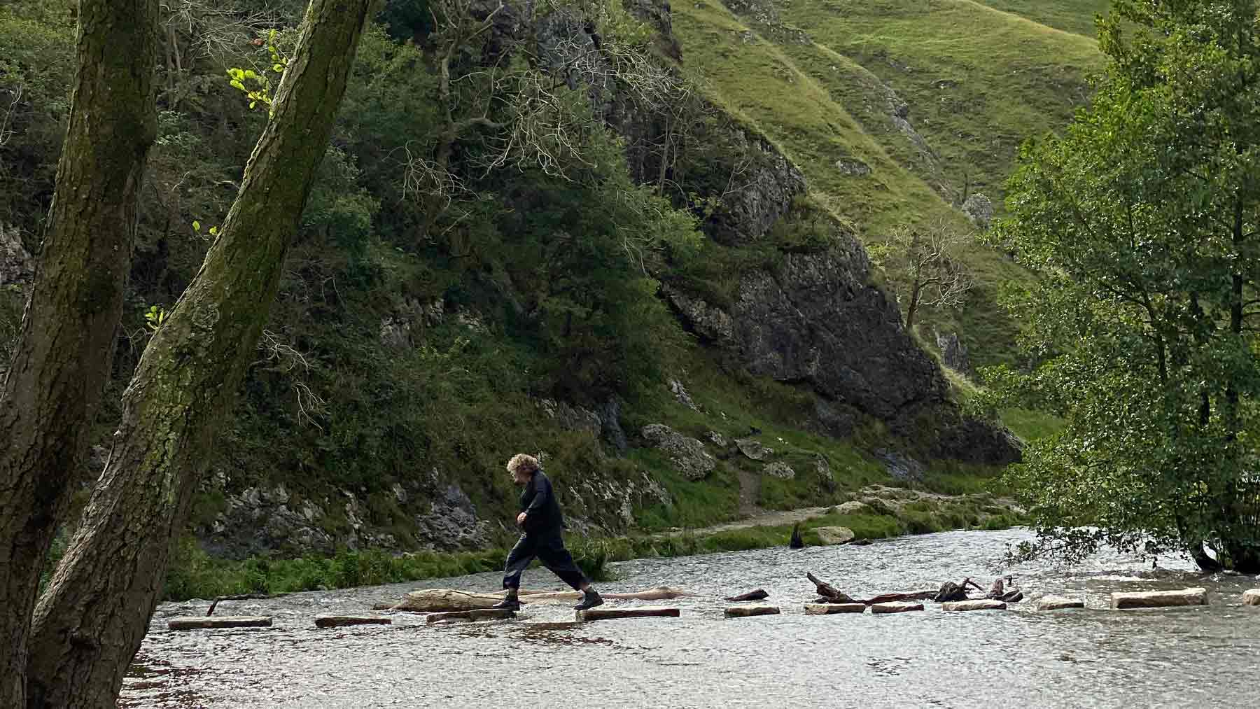 Clare wearing Asmuss jumping across the Dovedale Stepping Stones in the Peak District