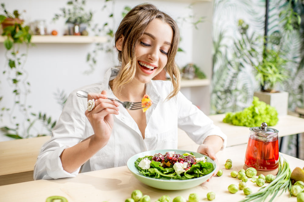 Young woman eating healthy food sitting in the beautiful interior with green flowers on the background