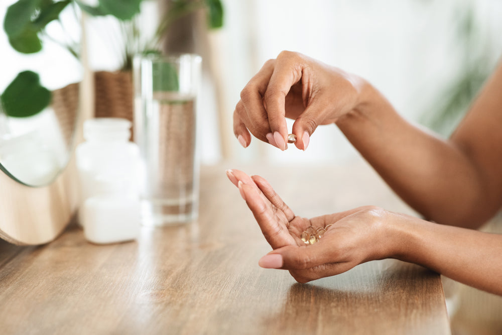 Unrecognizable African Woman Taking Beauty Supplements For Glowing Skin, Holding Omega-3 Fish Oil Capsules In Hands, Side View