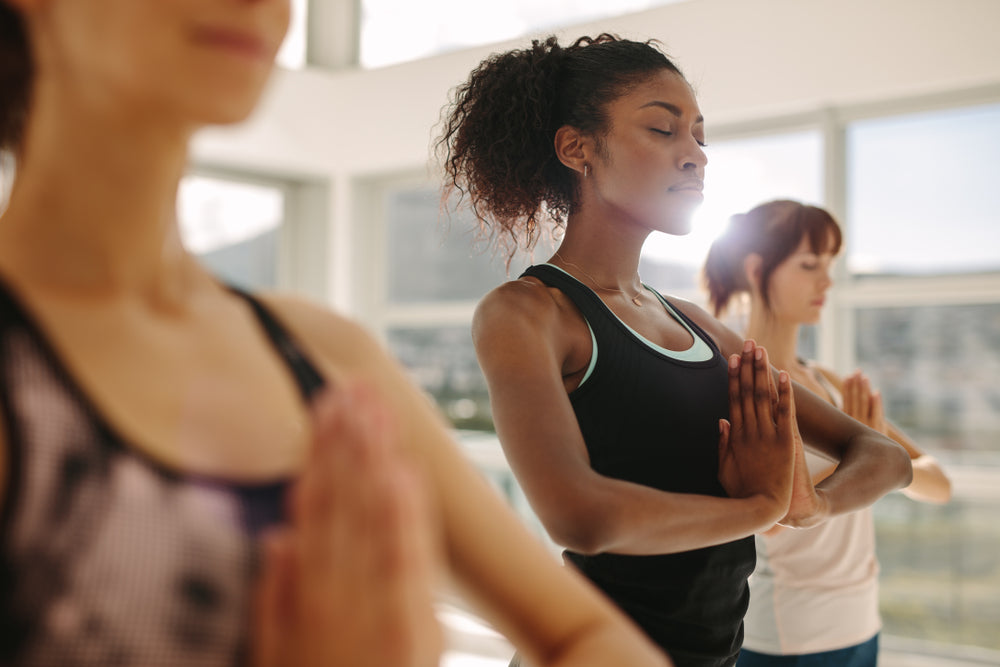 Fit young woman practice yoga with friends. Fitness female doing yoga meditation indoors in gym class.