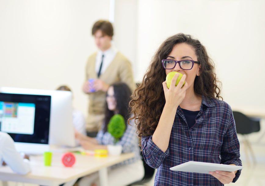 Portrait of pretty young woman eating an apple in her office.