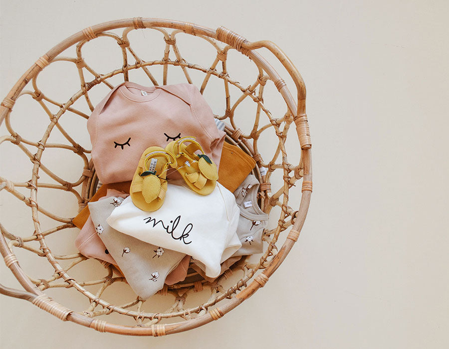 Baby bodysuits & playsuits in pink, white, oatmeal, stripes & yellow shoes in rattan laundry basket