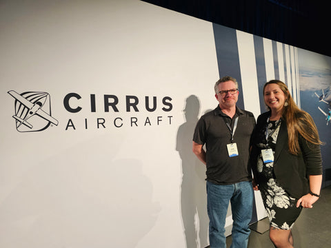 Dos empleados de SCS Interiors parados frente a un cartel de aviones Cirrus
