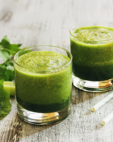 Two clear glasses filled with a green smoothie