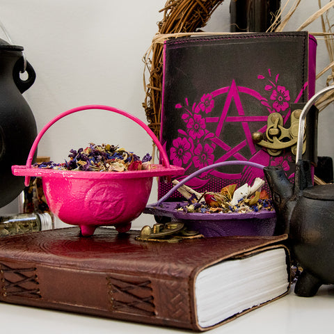Image of Pink Cast Iron Cauldron holding herbs on Leather-bound Grimoire
