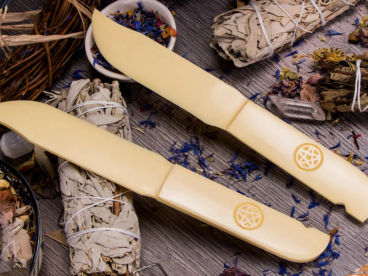 image of two acrylic ceremonial athames, the background features various herbs and two cleansing wands