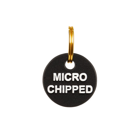 Black rubber mini charm tag with gold split ring, featuring the word 'MICROCHIPPED' to indicate a pet's microchip identification.