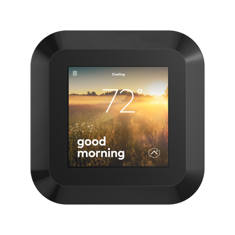 The smart thermostat from alarm.com with display screen active. On the screen there is an image of a grassy meadow in the morning, with the text "good morning" and text that indicates it is 72 degrees in the home.