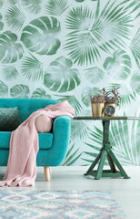 Light blue sofa with a rug in front, side table with a plant and clock on it, behind the sofa is a bold leafy accent wallpaper