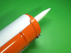 Orange caulk gun with white tube of caulk on a green background