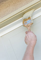 Hand holding a paint brush painting the trim of a door at an angle.