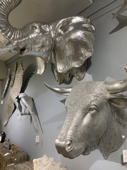 Large silver busts of an elephant and a bull hanging on a wall.