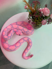 A pink snake accessory sitting on a table with some pink flowers next to it.