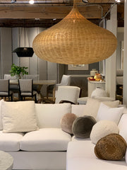 White sectional sofa with round ball pillows and above it is a large rattan light fixture.