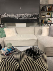 White sectional sofa, with a black and white cityscape photo behind it, and some cool geometric tables in front.