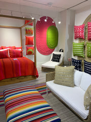 Canopy bed with hot pink bedding, an ottoman is in the forefront with colorful striped textile.