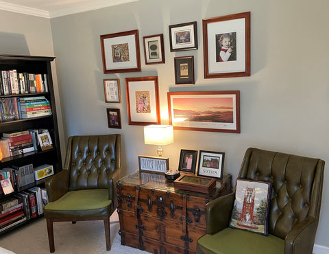 eclectic office space with bookshelf and placed wall art. two antique green leather chairs flanking an antique trunk.