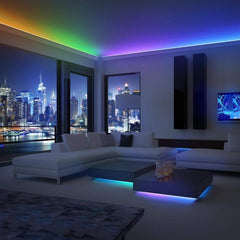 Living room with windows showing a city setting in the background, it's evening and there are neat LED lights in multiple colors along the wall molding and under the coffee tables
