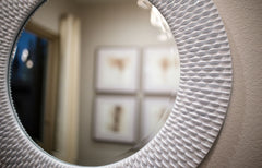 Close up of a round framed mirror on a wall, reflecting another wall with art on it.